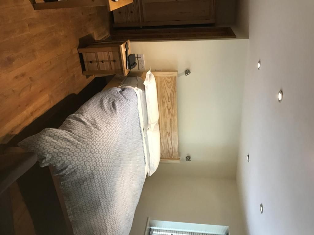 Une pièce avec un lit, une armoire en bois, un mur blanc et un luminaire au plafond.
