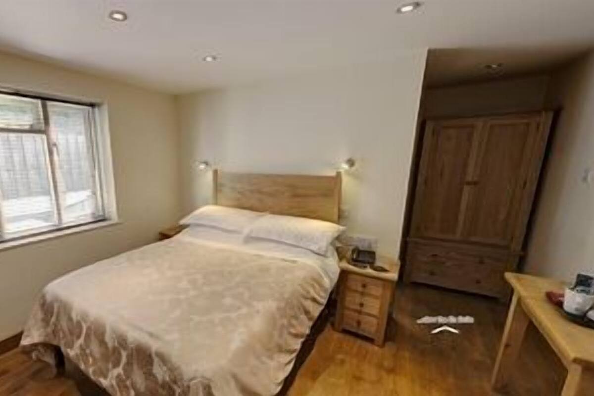 A bedroom with a bed, a nightstand, a wooden wardrobe, and a window.
