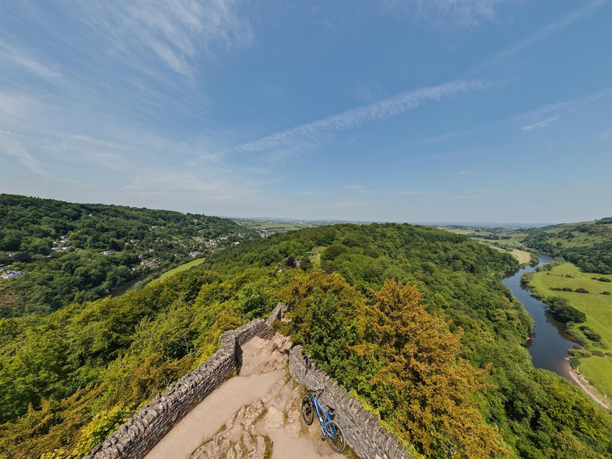 A stone pathway leading to a historic stone wall, surrounded by lush greenery and a river.