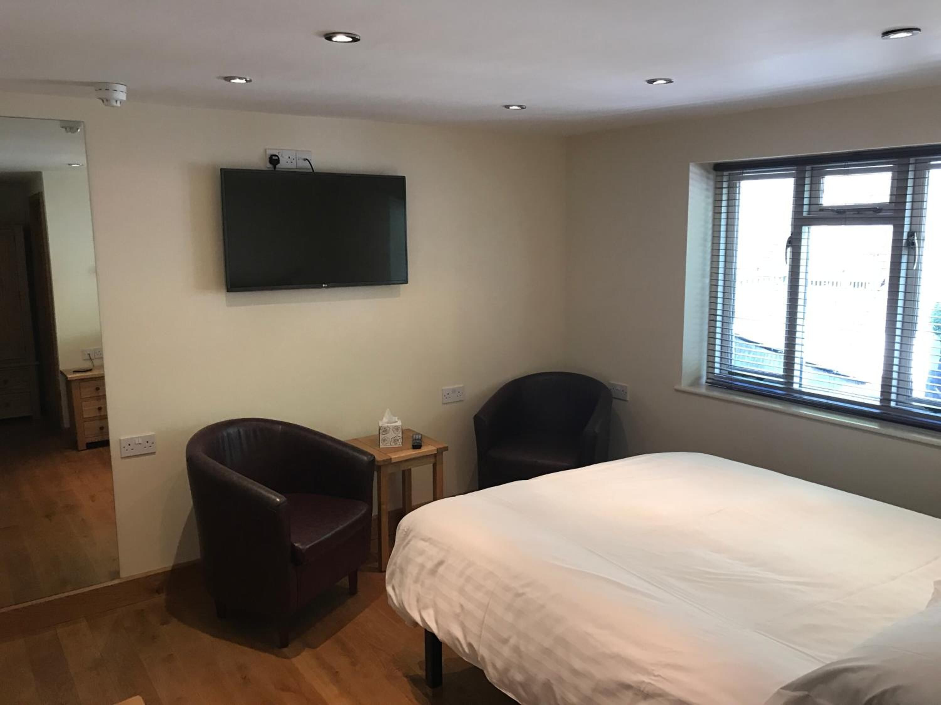 Un dormitorio con una cama, una silla, una mesita, un televisor y una ventana.