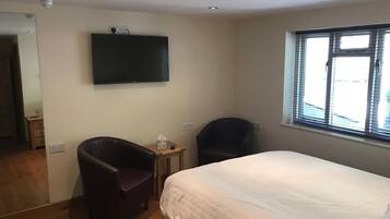 Un dormitorio con una cama, una silla, una mesita, un televisor y una ventana.