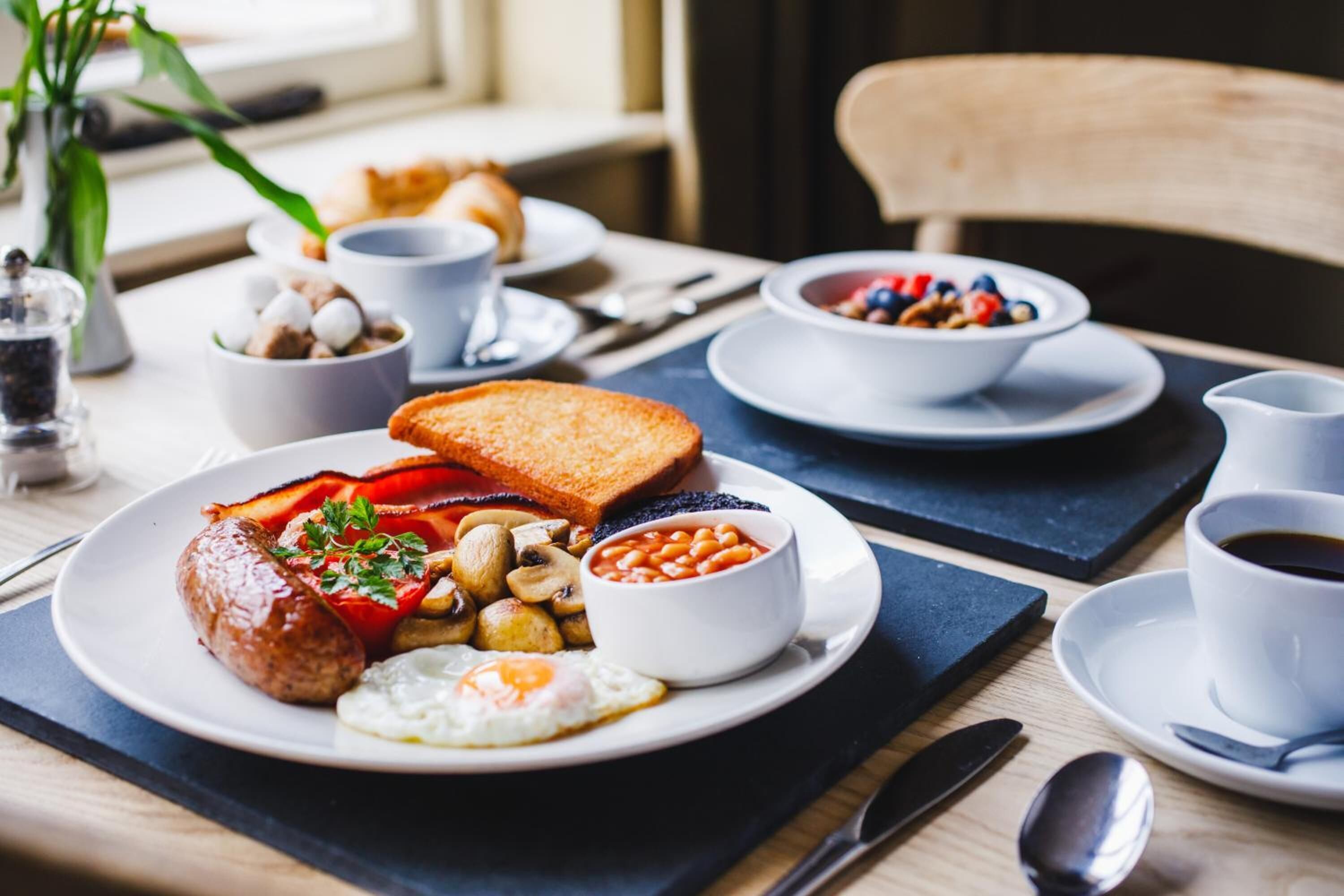 Ein Frühstückstisch mit Eiern, Würstchen, Toast, Bohnen und Pilzen.