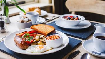 Ein Frühstückstisch mit Eiern, Würstchen, Toast, Bohnen und Pilzen.