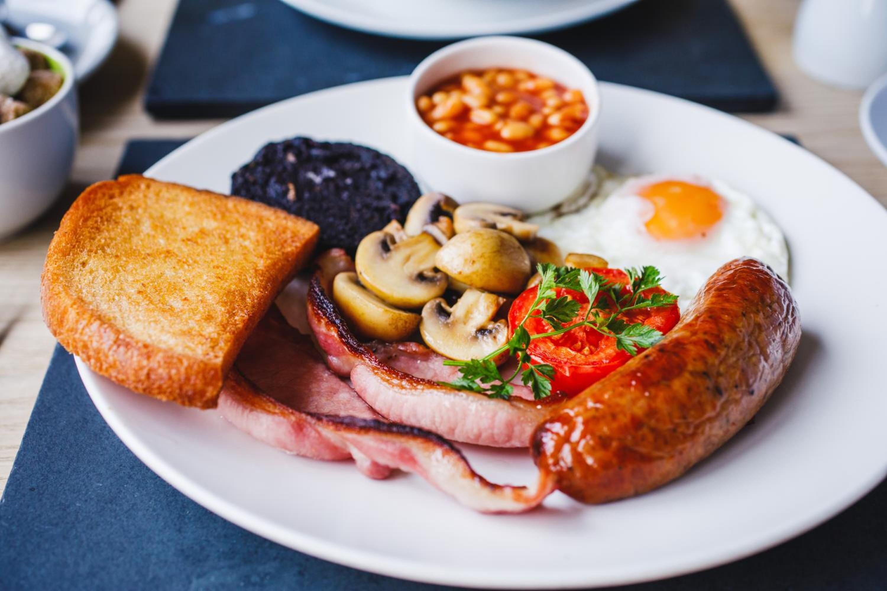 Une assiette comprenant des toasts, des champignons, du bacon, une saucisse, un œuf au plat et des haricots.