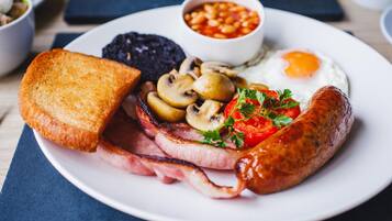 Une assiette comprenant des toasts, des champignons, du bacon, une saucisse, un œuf au plat et des haricots.