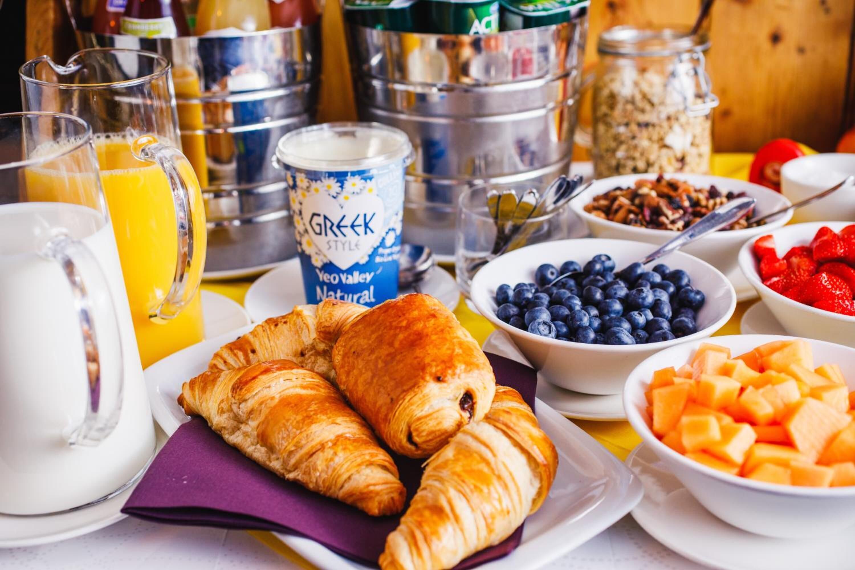 Desayuno con cruasanes, fruta y una lata de yogur griego.