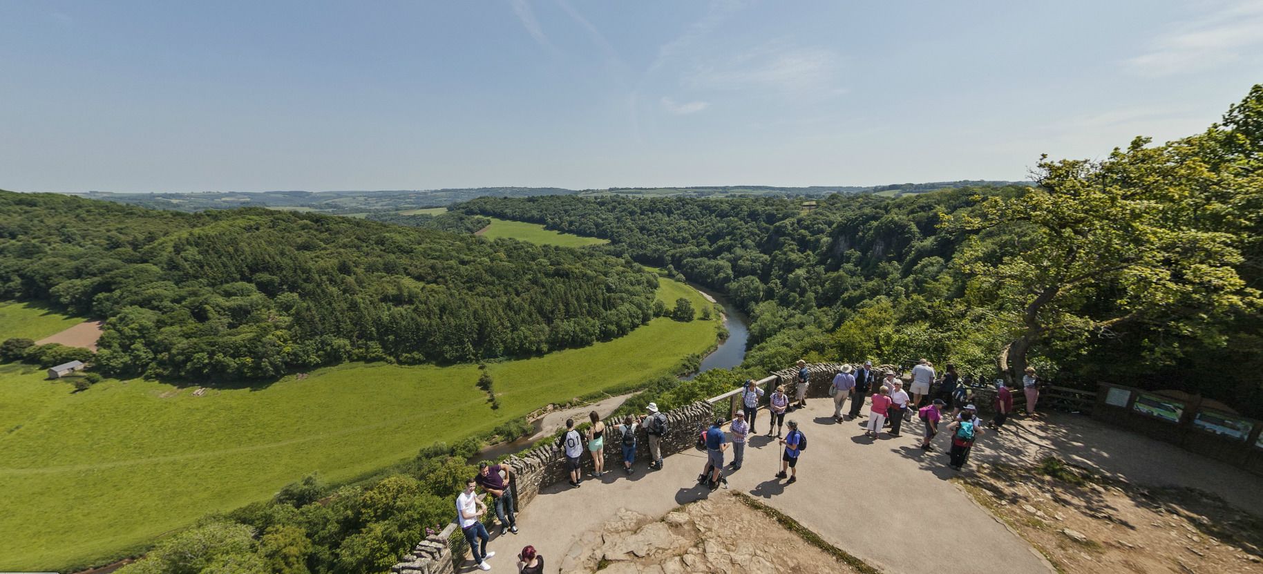 Eine Gruppe von Menschen steht auf einem Steinweg und blickt auf einen Fluss und grüne Felder.