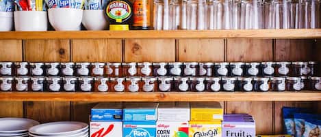 A kitchen shelf stocked with various food items including jars of preserves, boxes of cereal, and condiments.