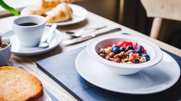 A breakfast setting with a bowl of cereal, a cup of coffee, and a croissant on a table.