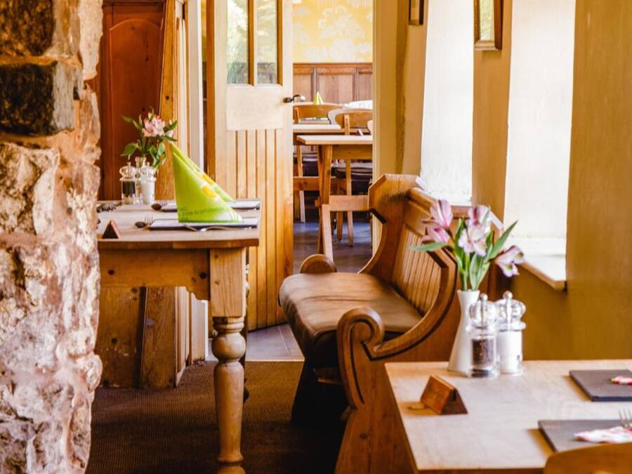 A rustic dining area with wooden furniture, a sign indicating the dining room, and a stone wall.