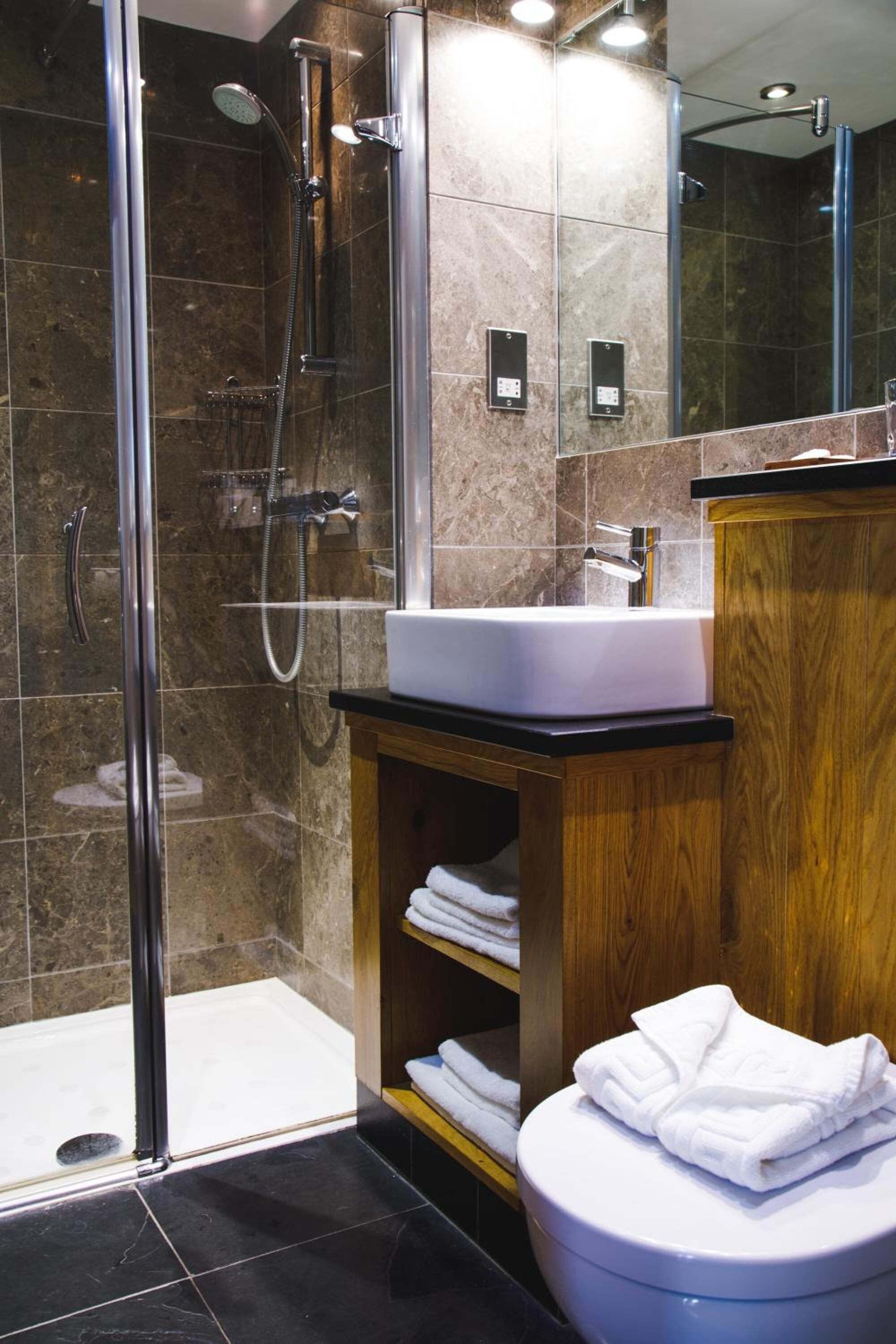A modern bathroom with a glass-enclosed shower, a white sink, and a wooden vanity.