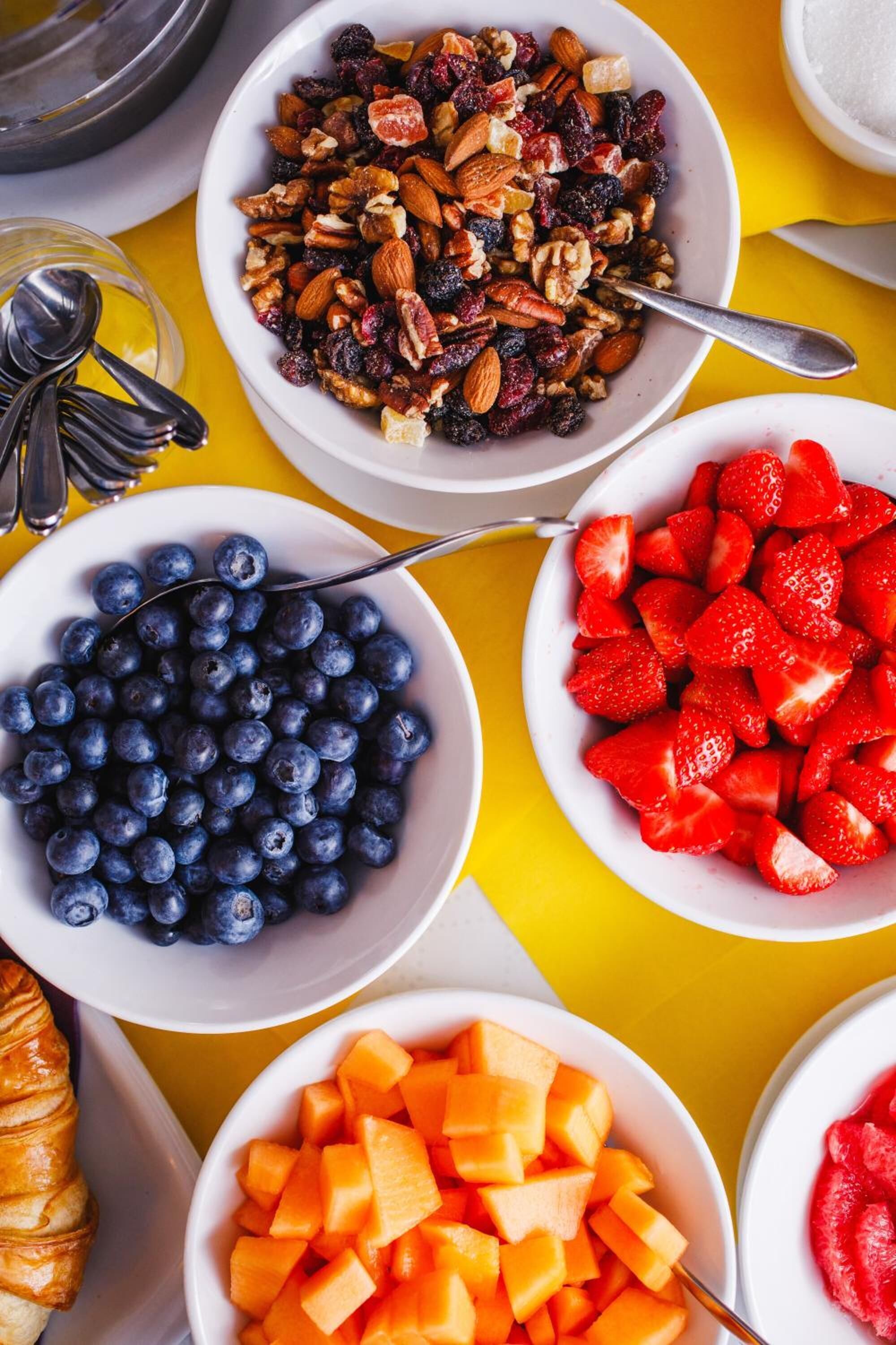 Ett frukostbord med skålar fyllda med blåbär, jordgubbar och honungsmelon, och en croissant.