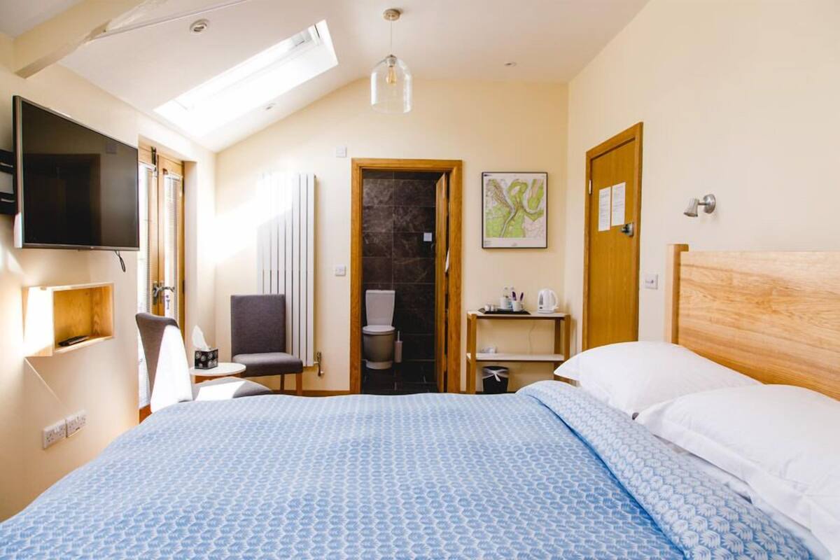 A hotel room with a bed, a desk, a chair, a television, a bathroom, and a wooden headboard.