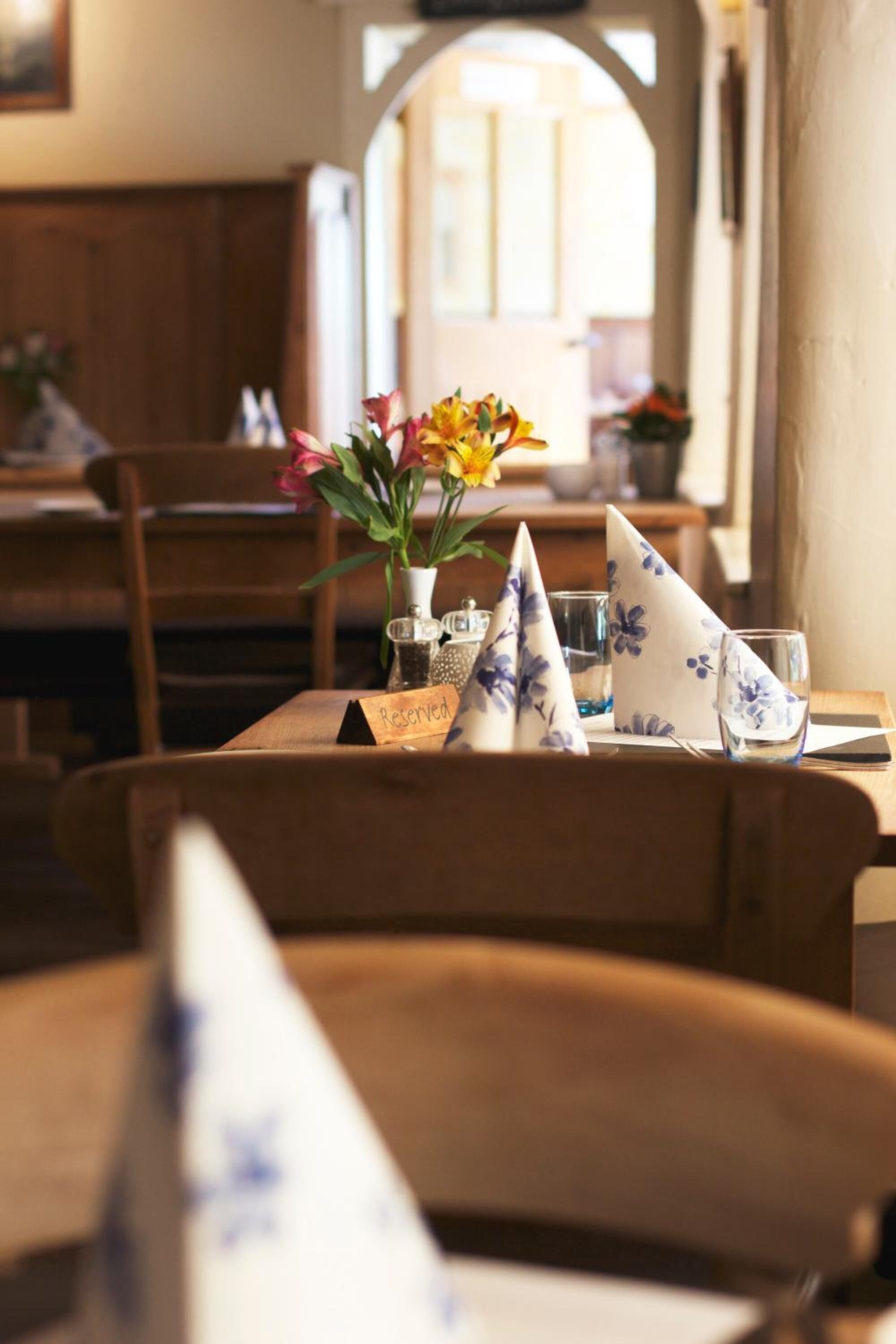 Een eettafel met een 'Gereserveerd'-bordje, een vaas met bloemen en een papieren servetjeshoedje.