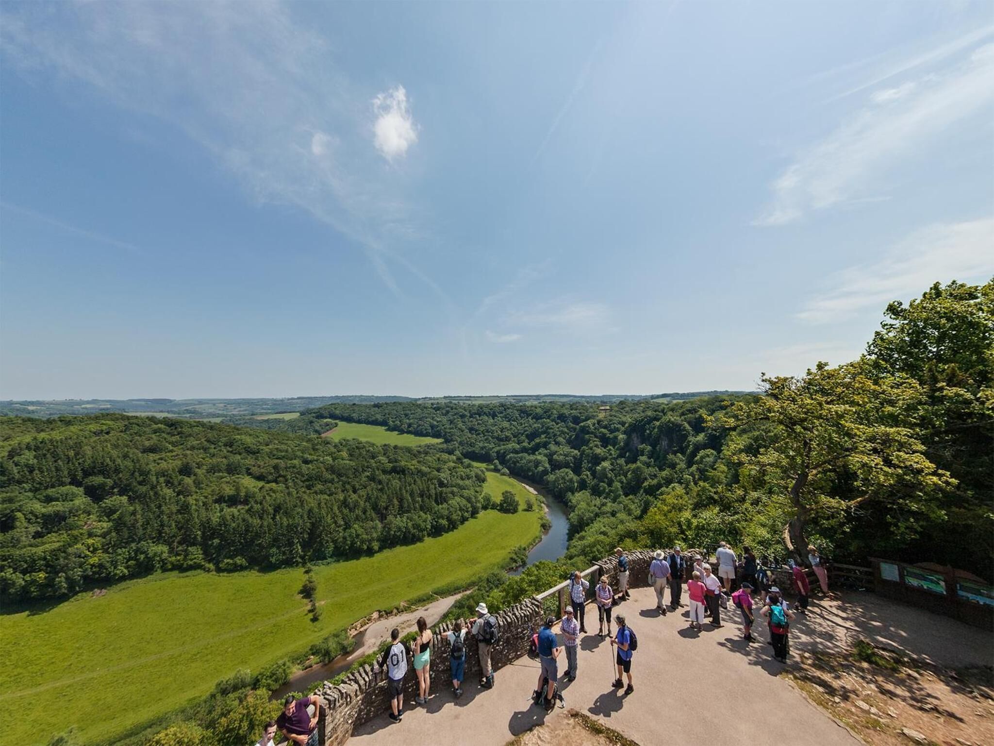 A group of people standing on a stone wall overlooking a river and forested landscape.