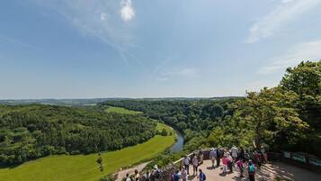 A group of people standing on a stone wall overlooking a river and forested landscape.