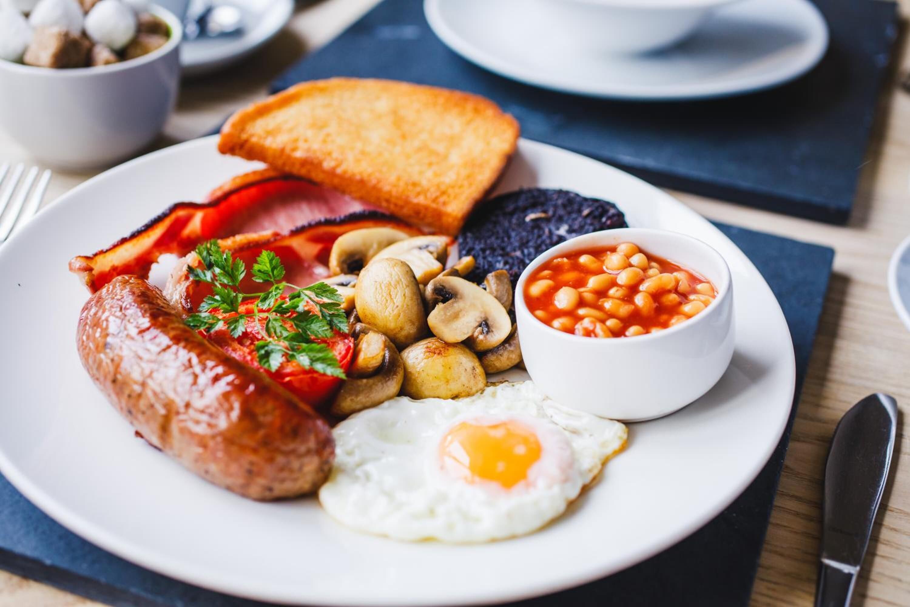 Un piatto di cibo per la colazione con pane tostato, uova, salsiccia, funghi, fagioli e pancetta.