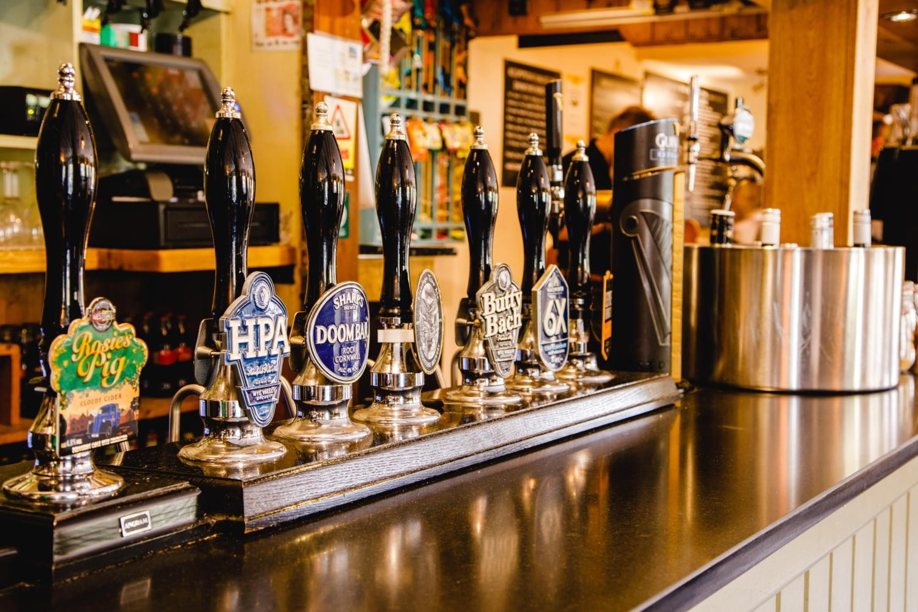 A bar counter with various beer taps, including brands like IPA, DOOMBAR, and 6X.