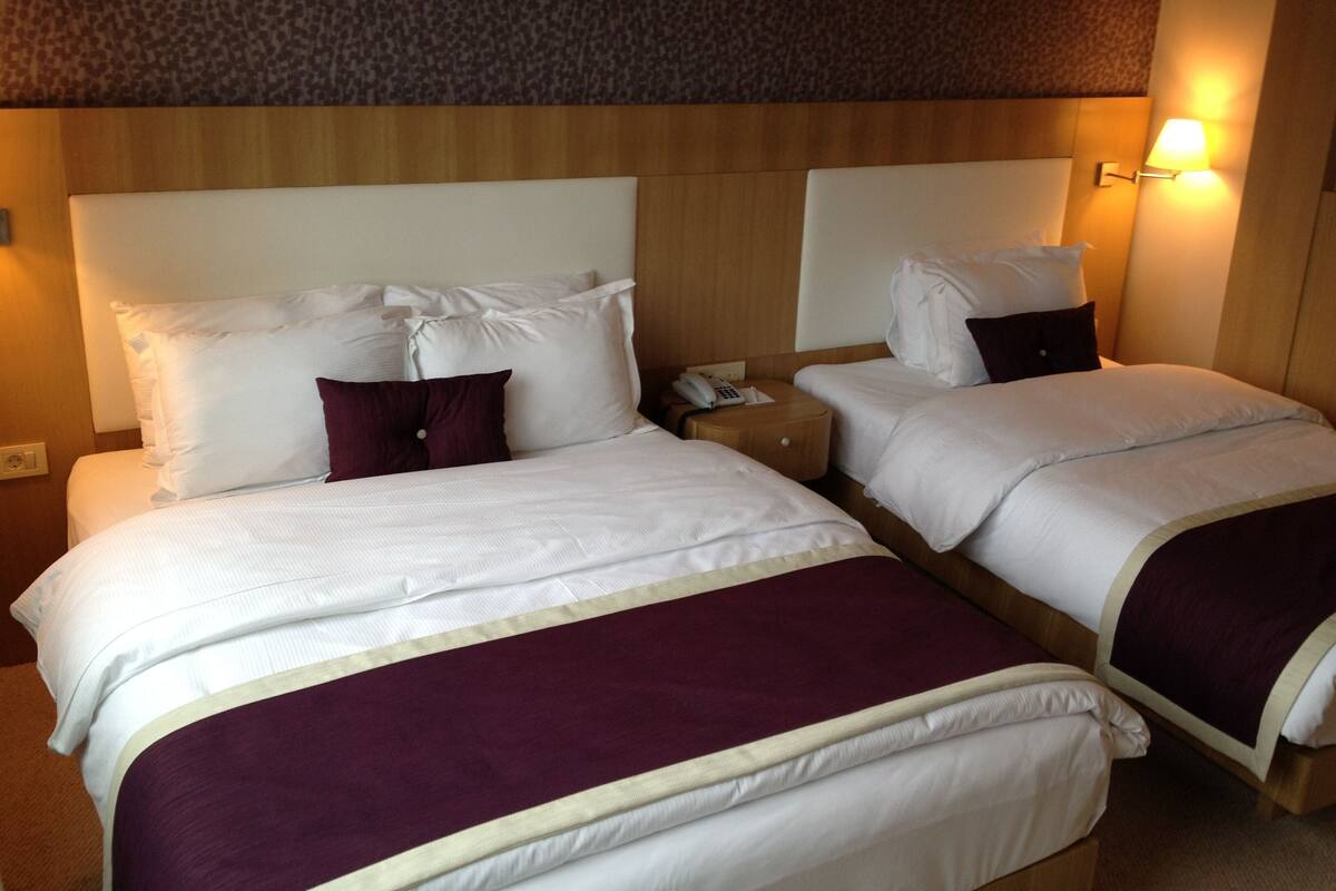 A hotel room with two beds, a wooden headboard, a nightstand with a phone, and a wall-mounted lamp.