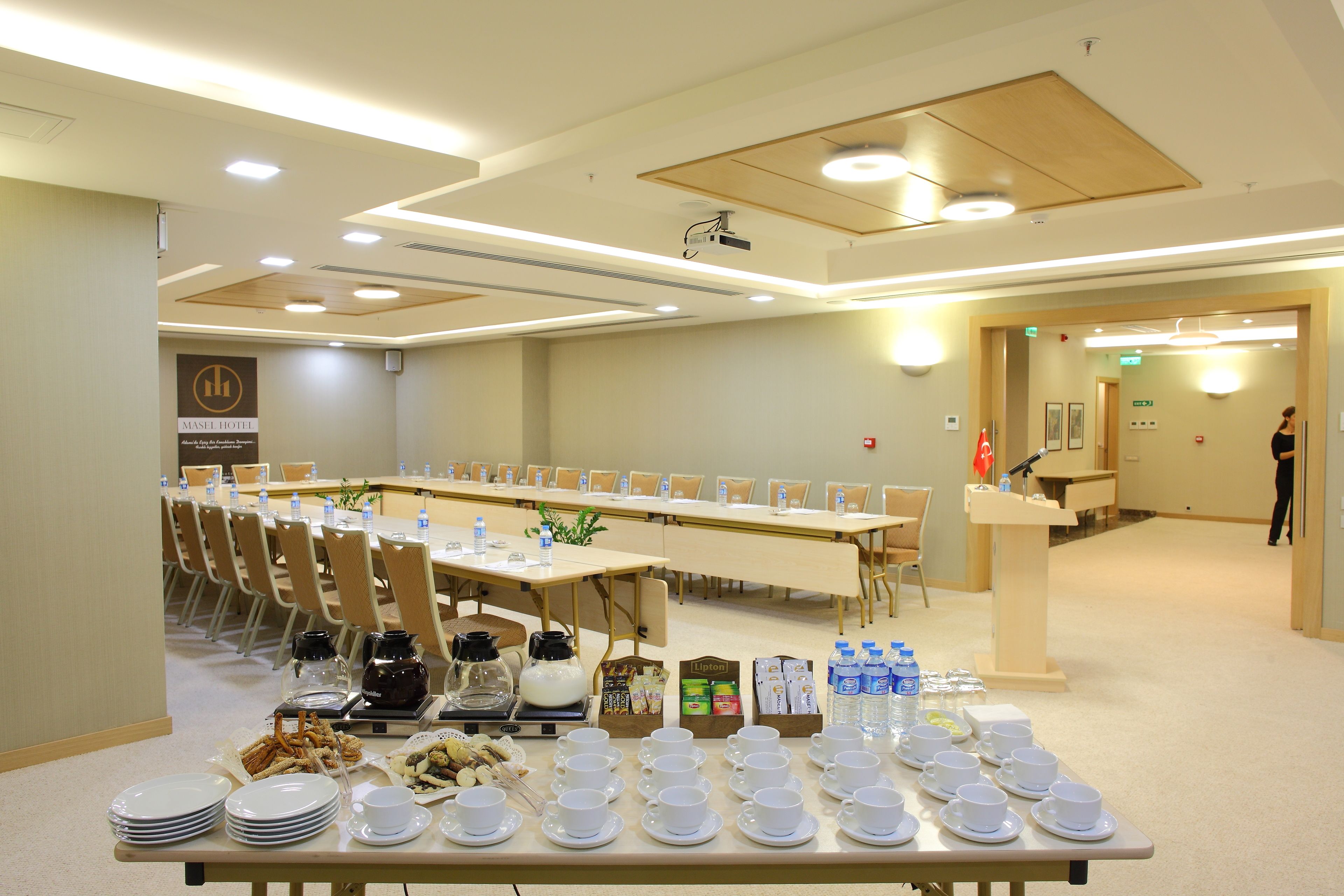 Une salle de conférence avec une longue table préparée pour une réunion, équipée de bouteilles d’eau, de gobelets et d’un projecteur.