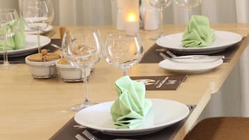 Una mesa de comedor bien dispuesta con platos, cubiertos y copas de vino, junto a una vela y un florero con flores.