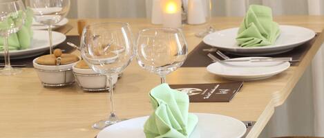 A neatly set dining table with plates, cutlery, and wine glasses, accompanied by a candle and a vase with flowers.