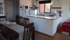 Uma cozinha compacta com uma ilha central, uma mesa de jantar com cadeiras e um micro-ondas sobre a ilha.