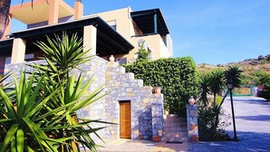 A modern building with a stone facade, a wooden door, and a well-maintained garden with various plants. - Wild Pear Villa (Malevizi)