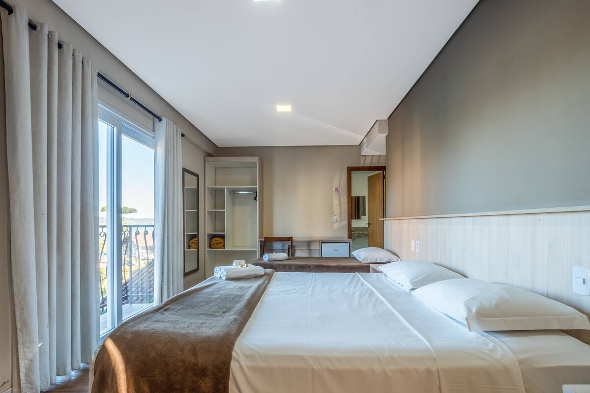 A hotel room with two beds, a wardrobe, a desk, and a balcony with curtains.