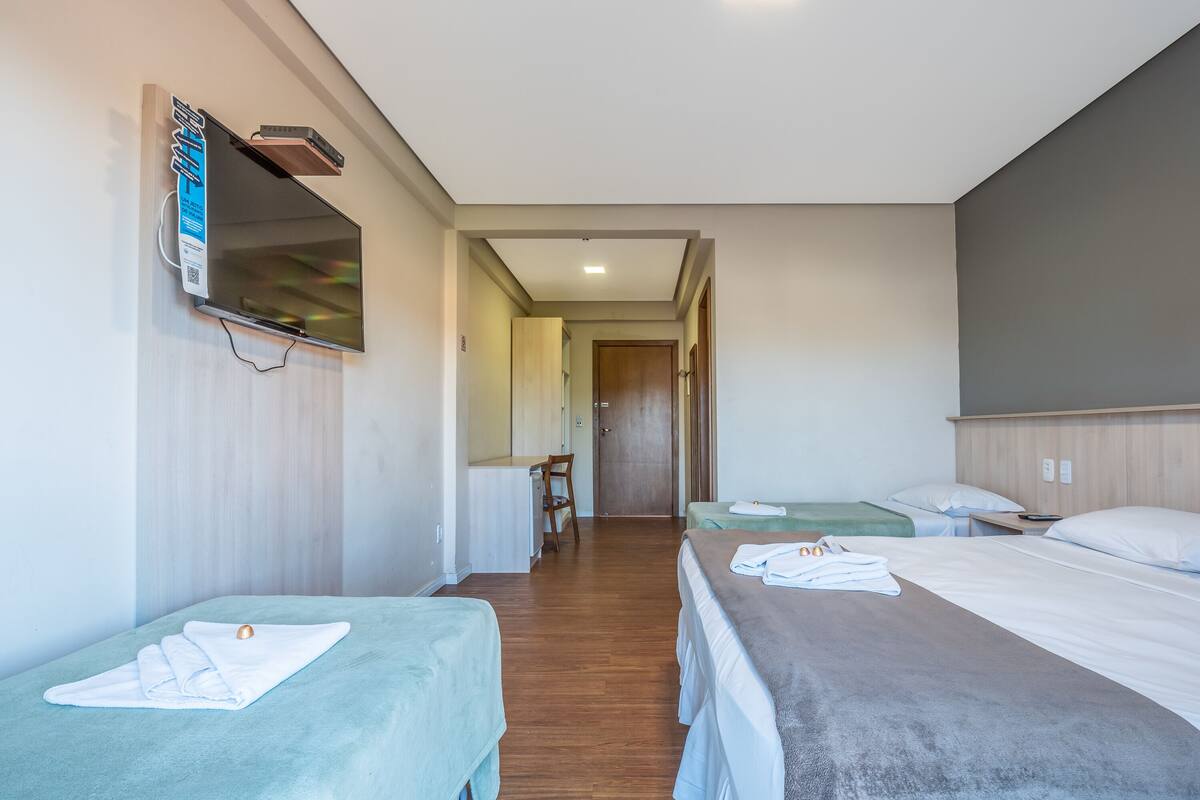 A hotel room with two single beds, a desk, a chair, and a television mounted on the wall.