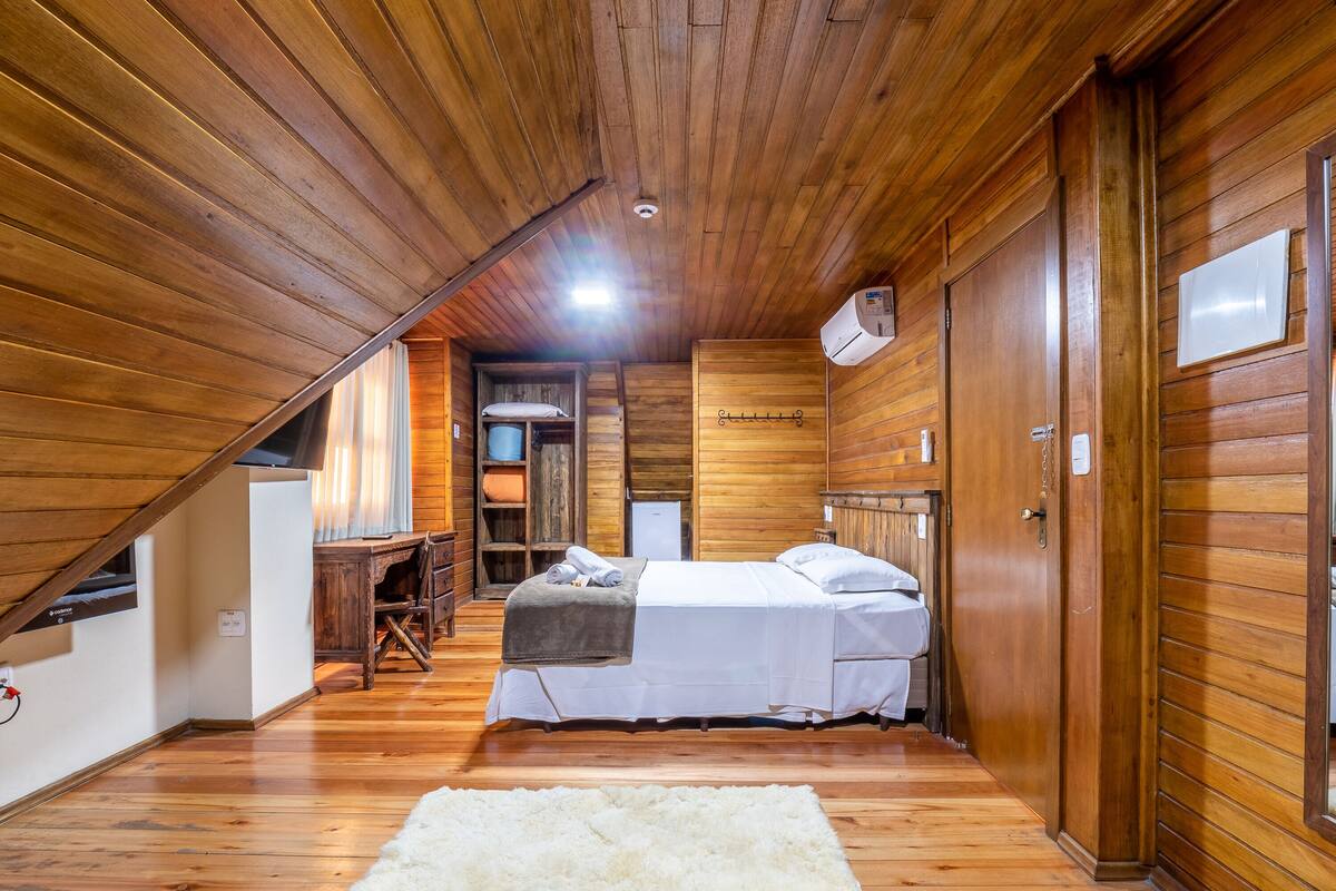 A wooden cabin bedroom with a bed, a desk, and a chair.