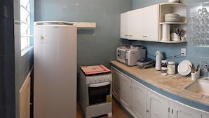 Uma cozinha compacta com geladeira, forno e micro-ondas. Há armários e bancada com diversos utensílios de cozinha.