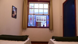Um quarto com duas camas, uma janela com cortinas, uma porta e um pequeno quadro na parede.