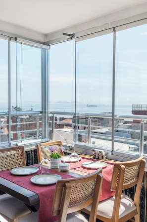 Comedor con mesa para cuatro, ventanas amplias con vista a la ciudad y barandilla de balcón.