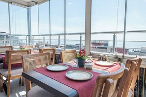 A dining area with tables set for four, large windows, and a view of the water. - Oban Suites İstanbul (Istanbul)