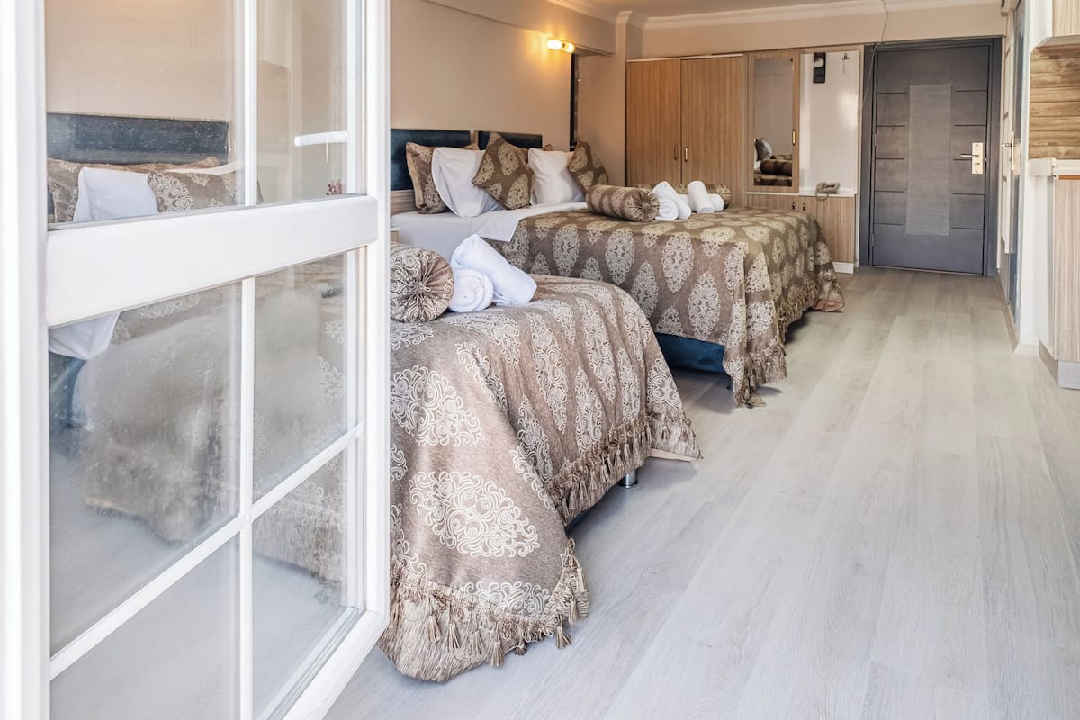 A hotel room with a large window, a bed with patterned bedding, a wardrobe, and a mirror.