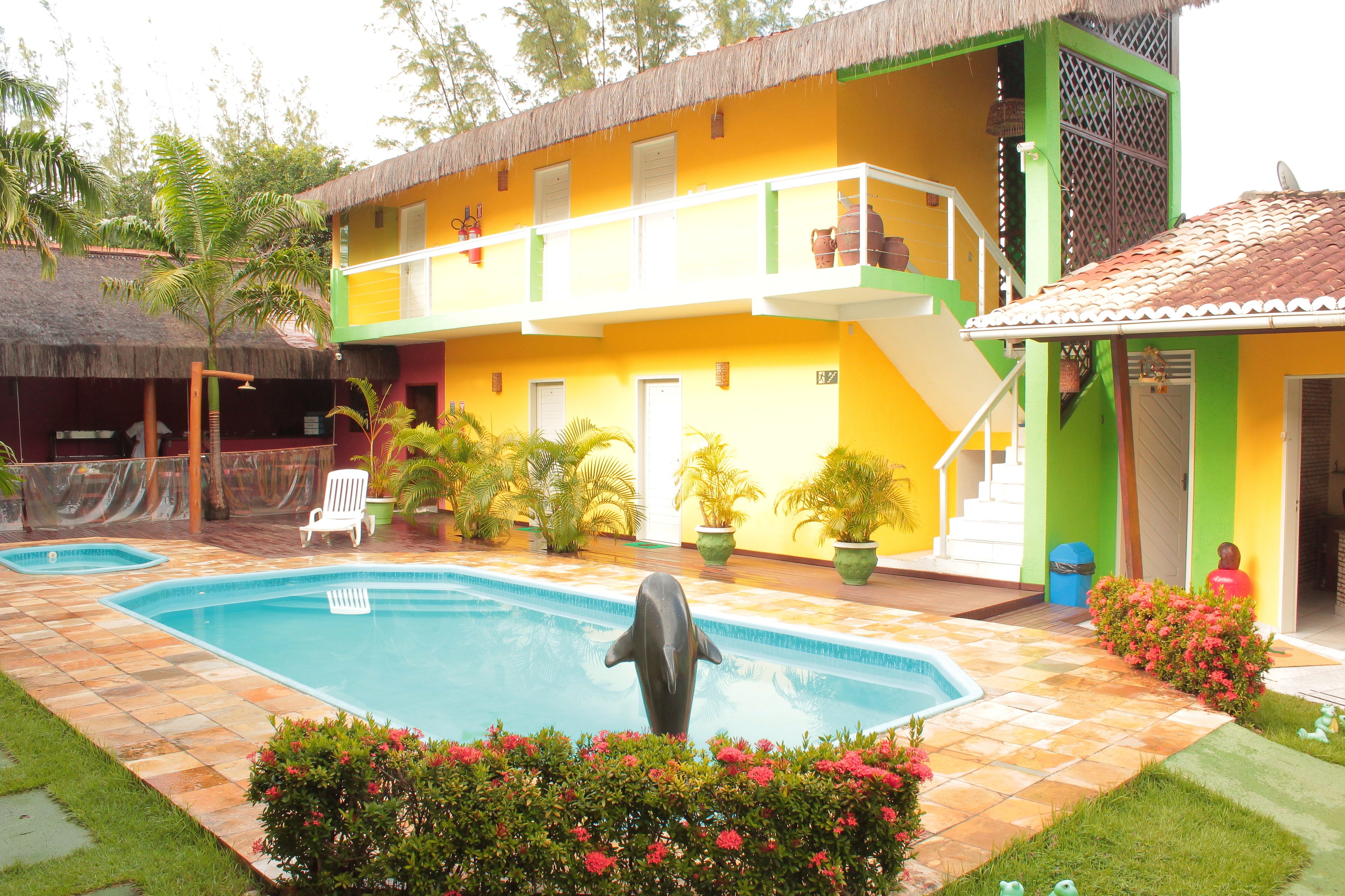 A two-story building with a swimming pool, a thatched-roof structure, and potted plants.