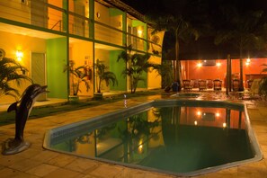 Una piscina con una escultura de delfín, rodeada de palmeras y mobiliario exterior.