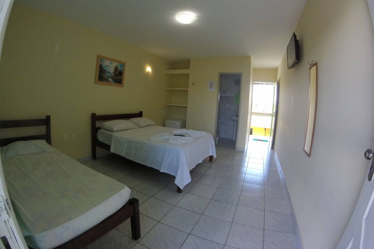Una habitación de hotel con dos camas individuales, un baño pequeño y un pasillo que conduce a otra habitación.