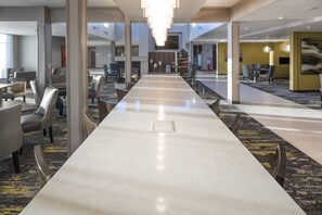 A spacious hotel lobby with a long reception desk, multiple seating areas, and a high ceiling with natural light.