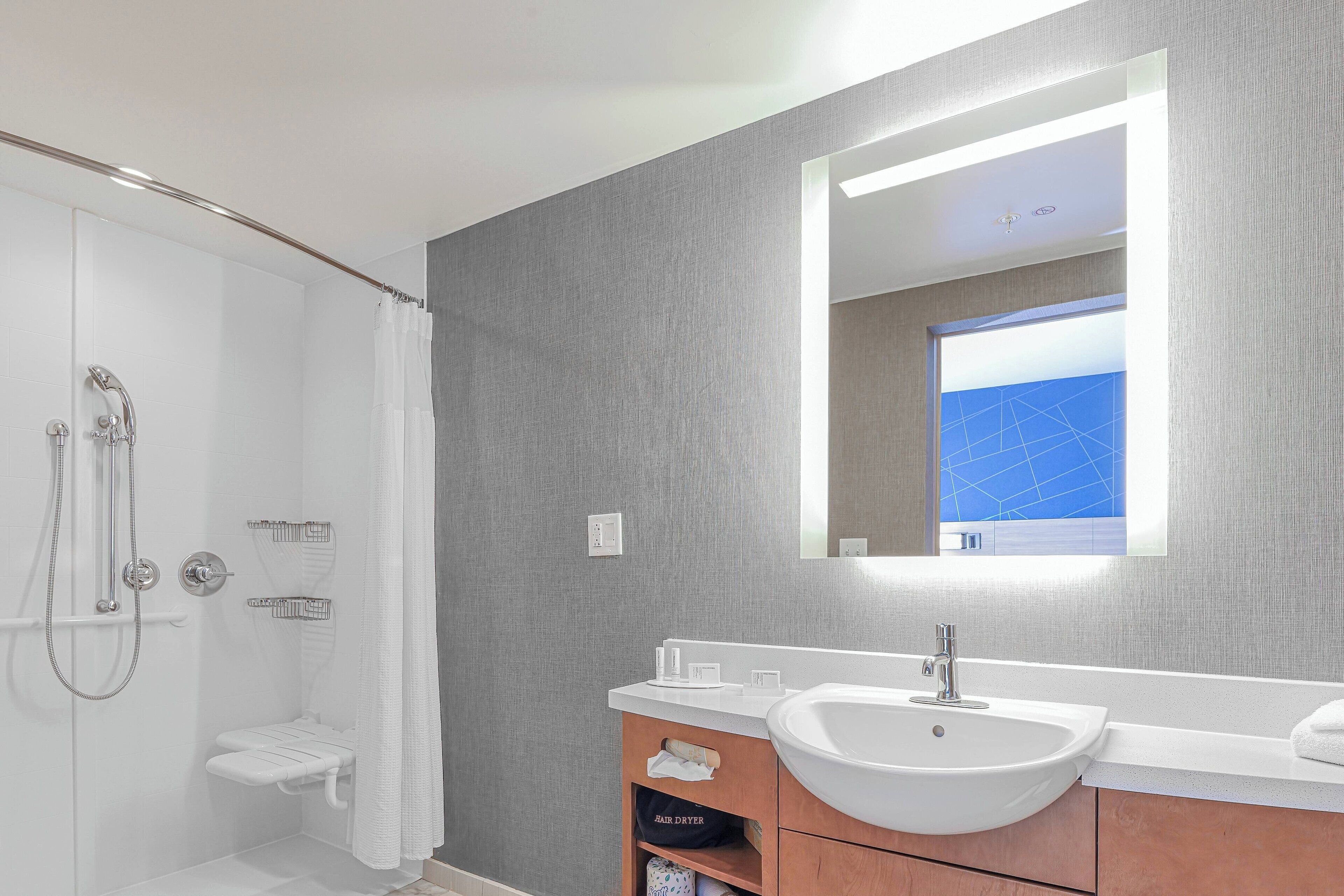 A modern bathroom with a walk-in shower, a large mirror, and a white sink.