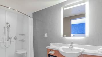 A modern bathroom with a walk-in shower, a large mirror, and a white sink.