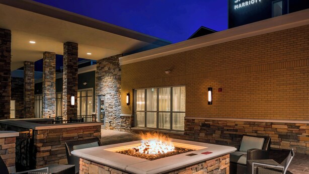 An outdoor patio area with a stone fire pit, seating, and a Marriott sign in the background. - SpringHill Suites by Marriott Fishkill (Fishkill)