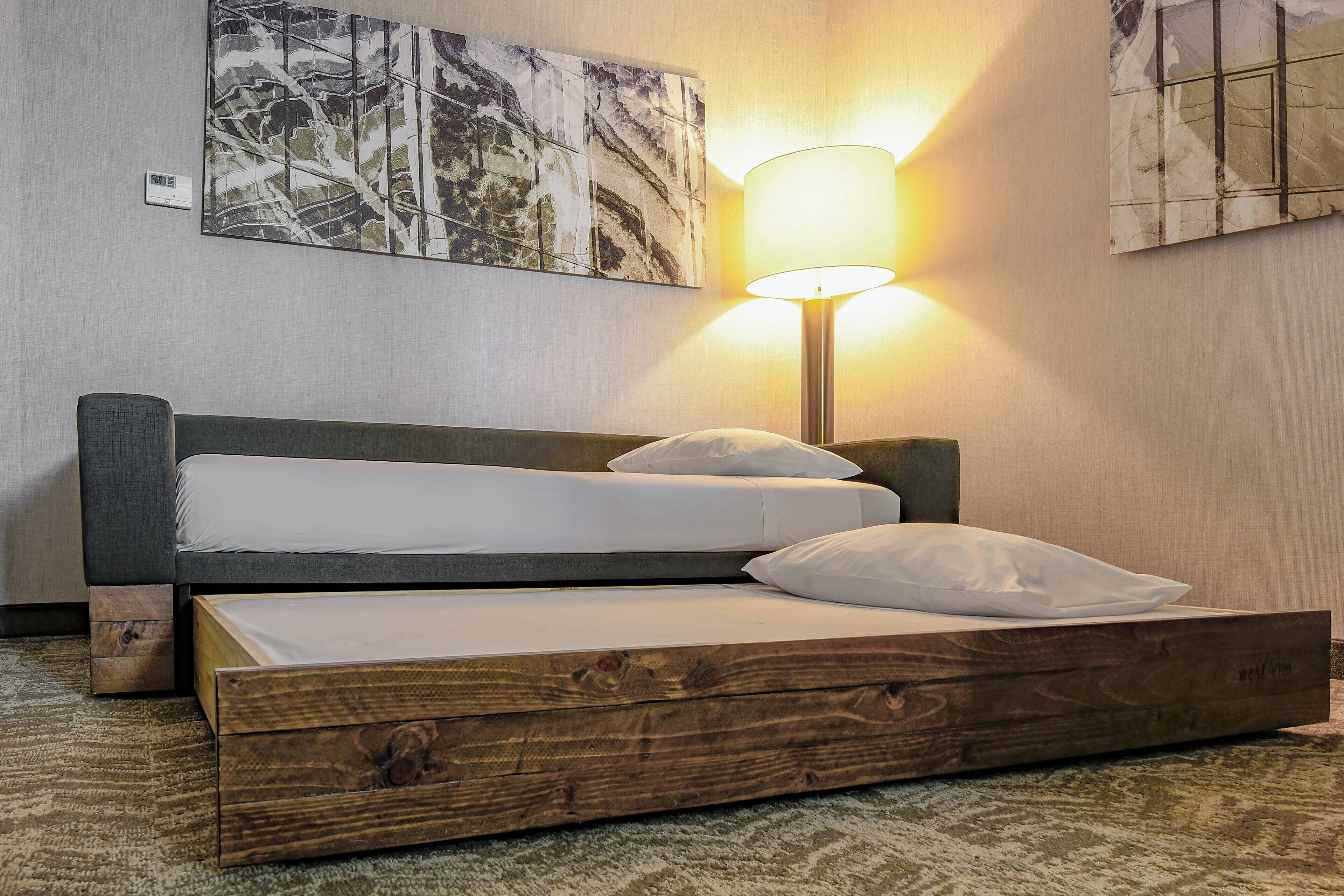 A bed with a wooden frame, white bedding, and a wall-mounted lamp.