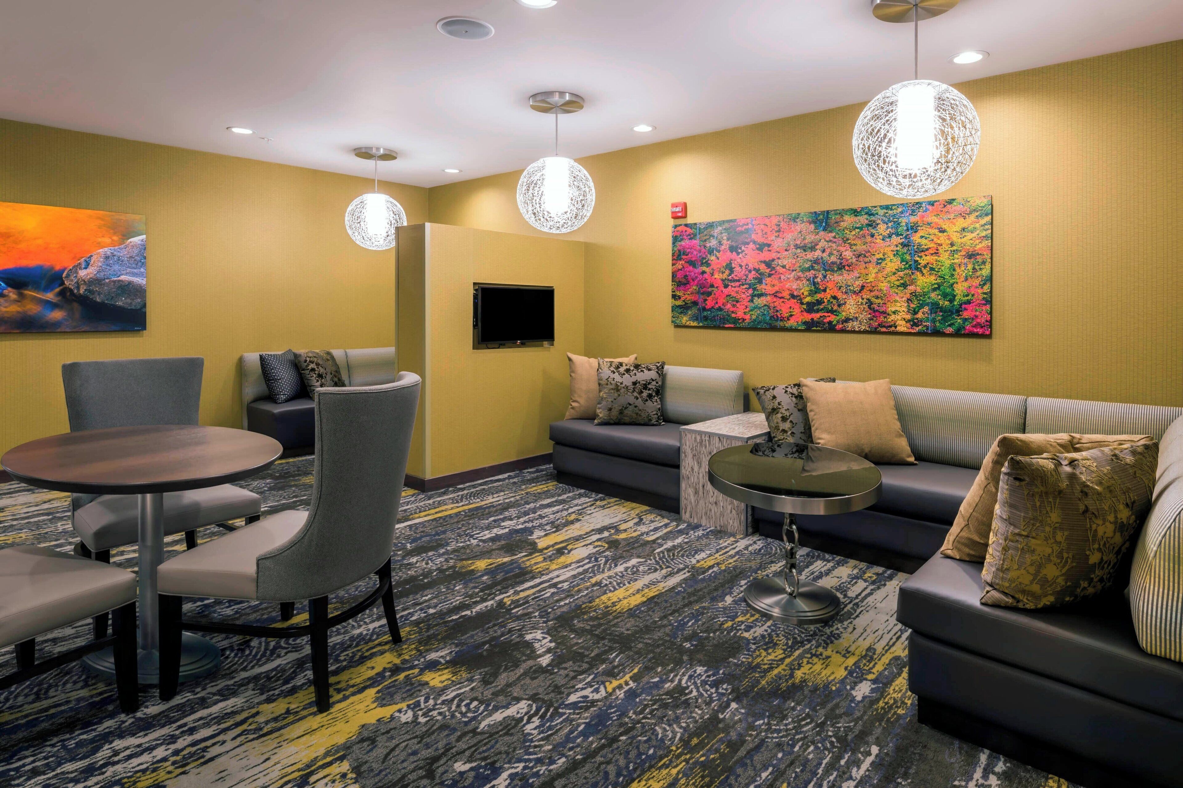A hotel lobby with a sofa, chairs, a table, and a TV.