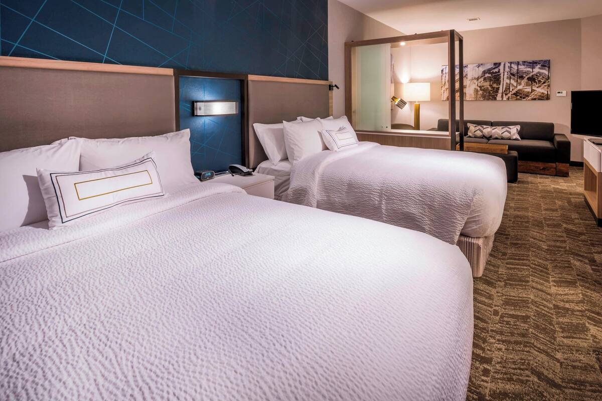 A hotel room with two beds, a desk, a TV, and a painting on the wall.