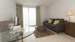 A modern living room with a glass dining table, a sofa, and a lamp. - Citystay Living - Mill Park Apartments (Cambridge)