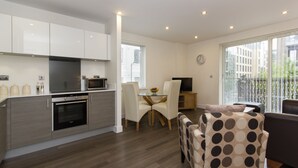A modern kitchen with white cabinets, a built-in oven, and a dining area with a glass table and chairs. - Citystay Living - Mill Park Apartments (Cambridge)