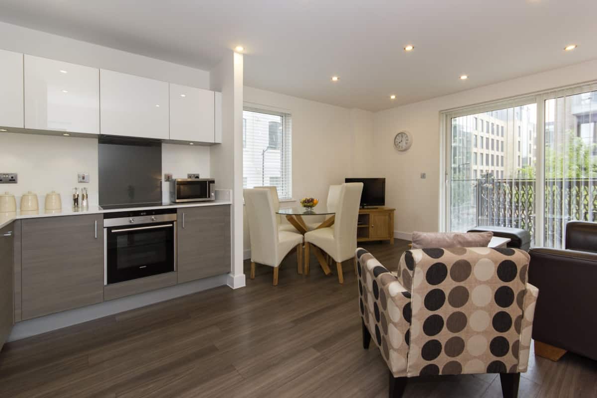 A modern kitchen with white cabinets, a built-in oven, and a dining area with a glass table and chairs.