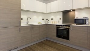A modern kitchen with light wood cabinets, stainless steel appliances, and a central island. - Citystay Living - Mill Park Apartments (Cambridge)